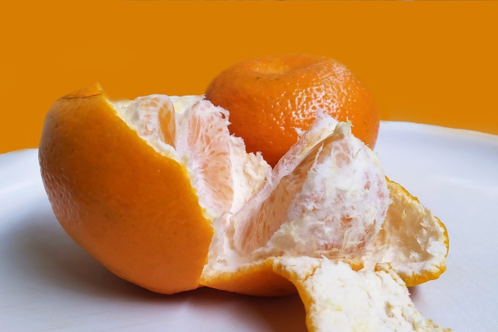 An orange on a plate, partially peeled and split open
