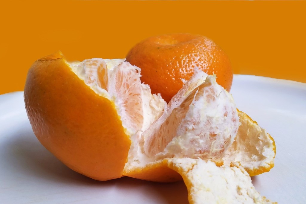 An orange on a plate, partially peeled and split open