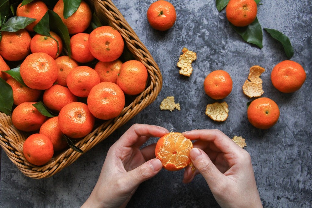 A person with a basket of oranges, peeling them.