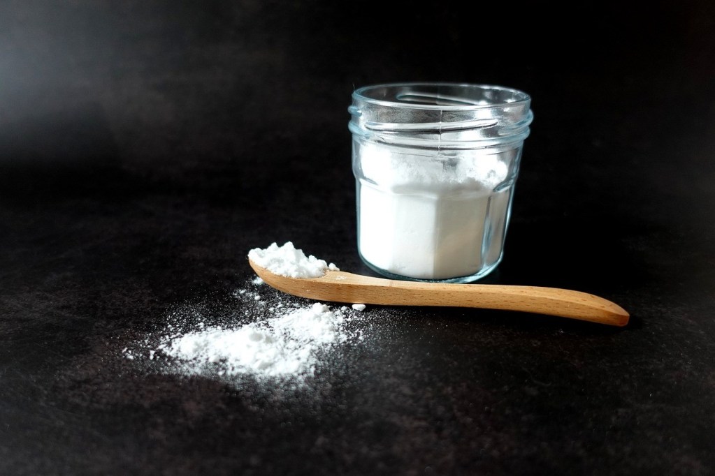 A white powder in a glass jar and a wooden spoon on a black background
