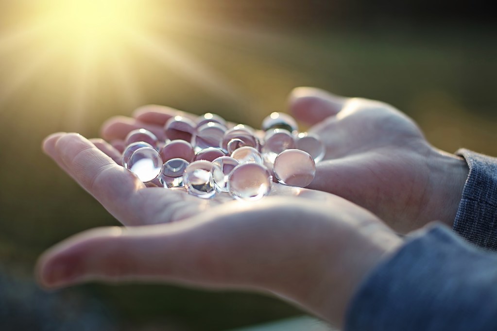Hands holding clear water beads in the sun