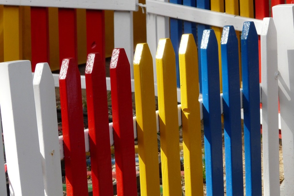 A wooden picket fence painted white, red, yellow, and blue in a repeating pattern.