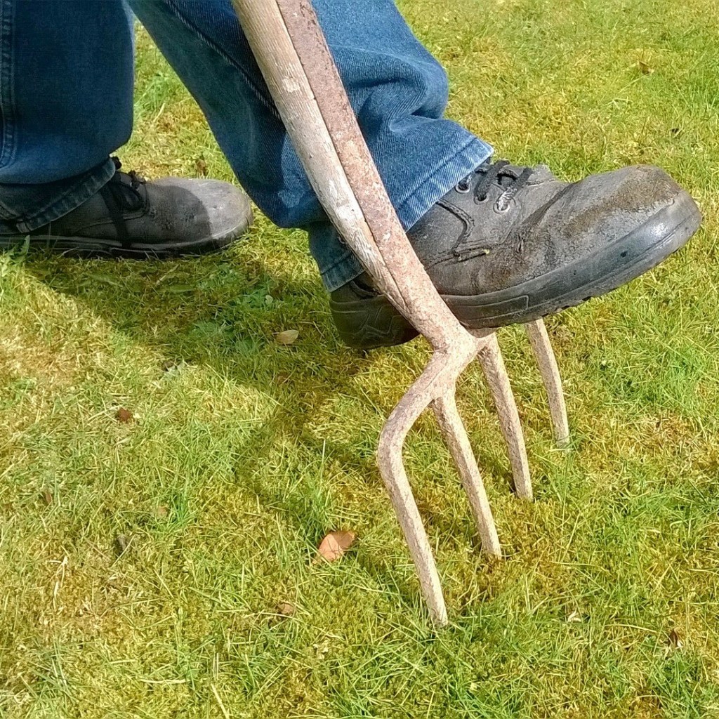 A person digging into grass with a garden fork