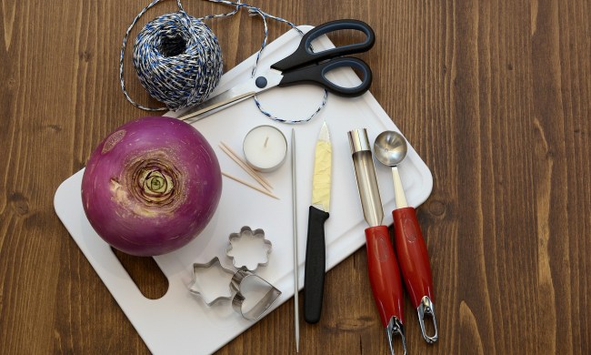 A beet on a table with carving tools, including scissors, strings, knives, and a small candle