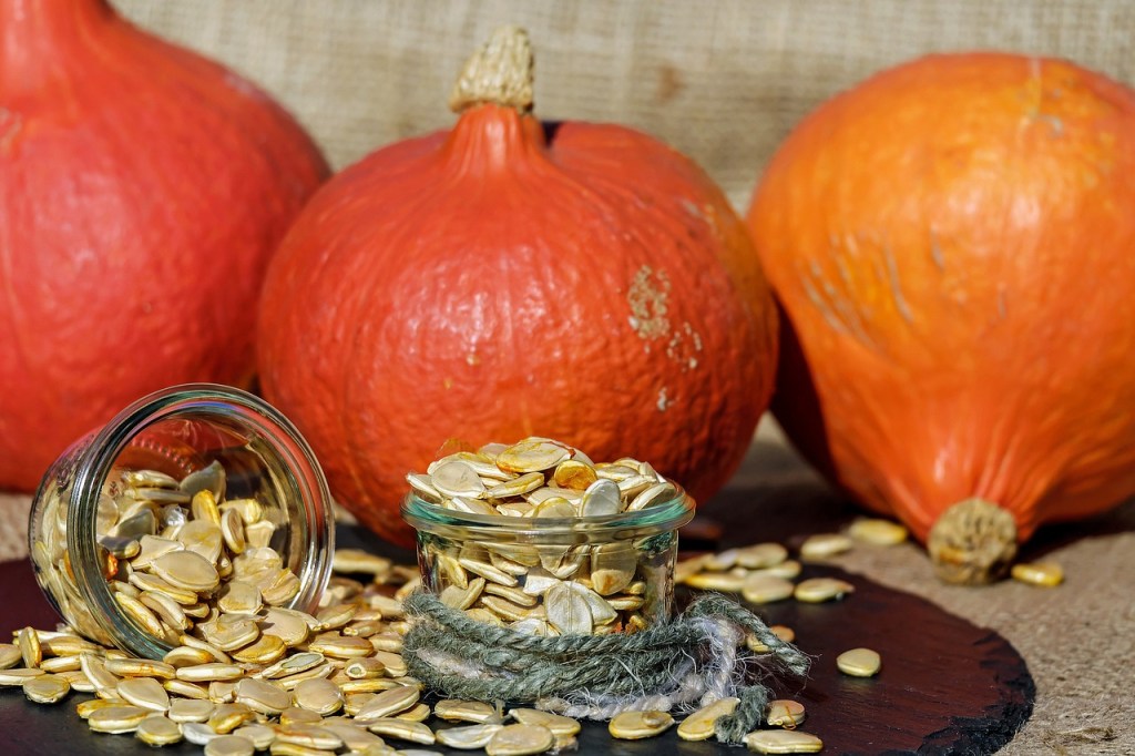 3 orange pumpkins and 2 glass jars of pumpkin seeds