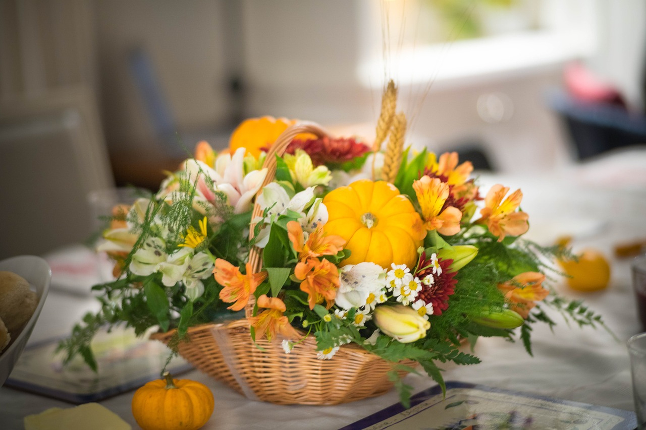 A thanksgiving table display of flowers and small pumpkins in a basket
