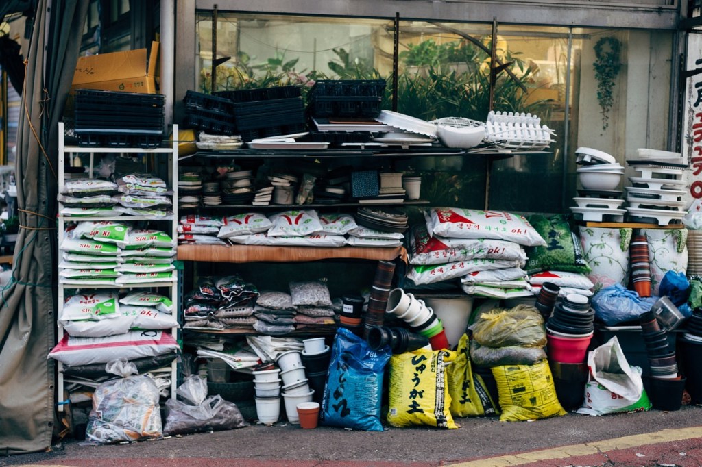 An outdoor shelf with fertilizer, soil, and flower pots